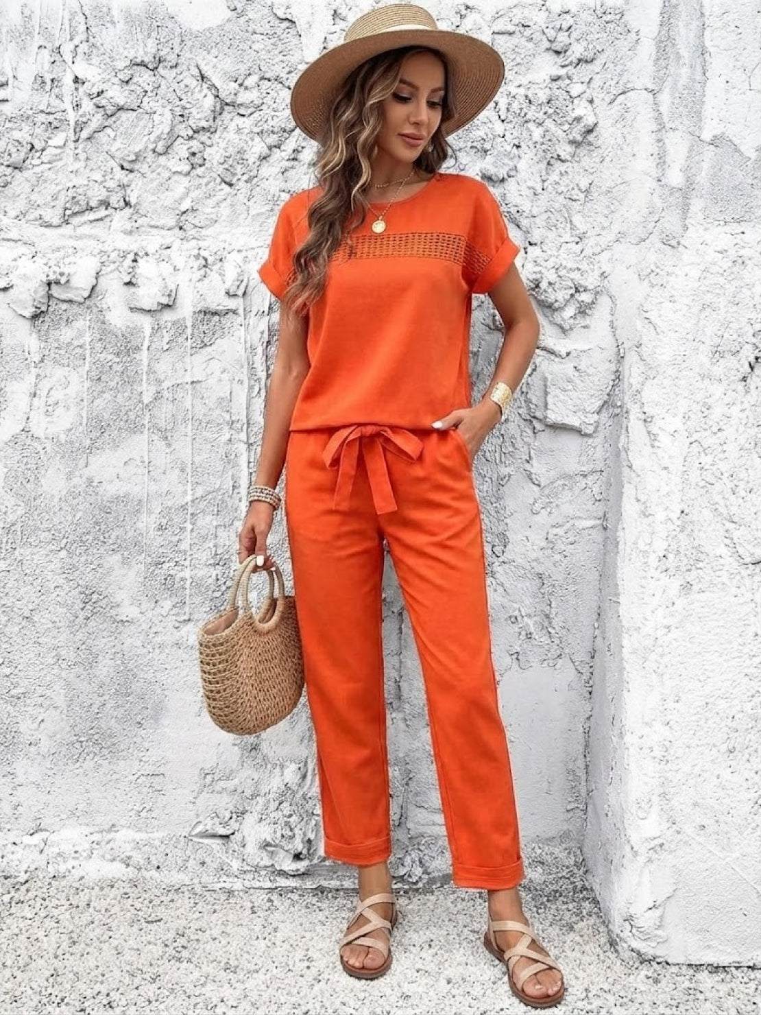 woman wearing orange 100 cotton total comfort two-piece travel set with hat and woven bag against textured white wall
