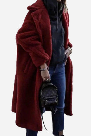 Woman wearing a loose fit glamour teddy coat in deep red with casual black hoodie and jeans, holding a small black backpack