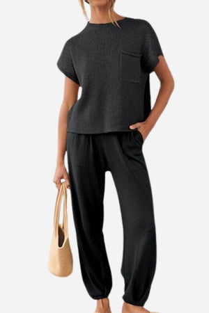 Woman wearing black Comfy Couture Knit Sweater two-piece set with short-sleeve pullover and high-waisted pants holding beige handbag