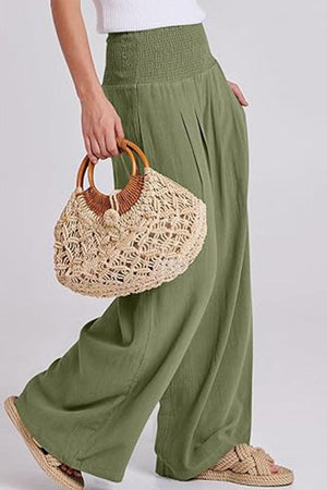 Green palazzo pants with smocked waistband paired with woven handbag and sandals.