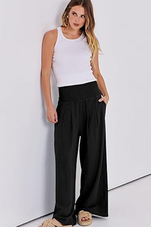 Woman wearing black oversized palazzo pants with a white sleeveless top against a white background