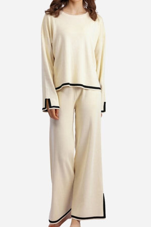 Woman wearing cream long sleeved relaxed fit lounge two-piece set with black trim on cuffs, hem, and pant edges