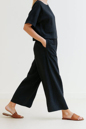 Woman wearing black loose fit co-ord set with wide-leg trousers and relaxed top, paired with brown slide sandals