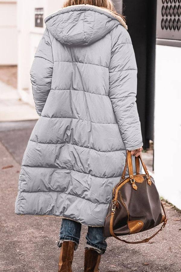 Long gray Sherpa-lined hooded teddy coat with puffer design worn by woman carrying brown handbag outdoors