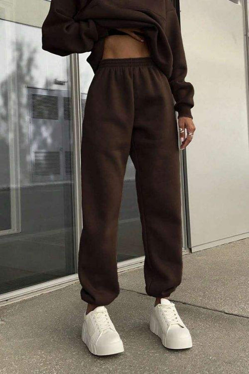 Woman wearing brown cotton-blended two-piece tracksuit pants with white sneakers outdoors.