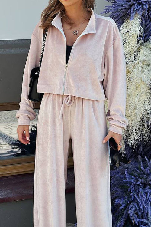 Woman wearing a soft pink zip up cropped sweatshirt and wide leg velour pants leisure two-piece co-ord set.