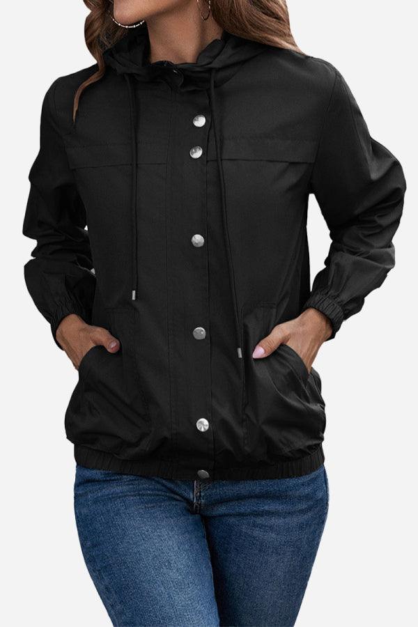 Black outdoor hooded raincoat and windbreaker with button closure and elastic cuffs on woman wearing jeans