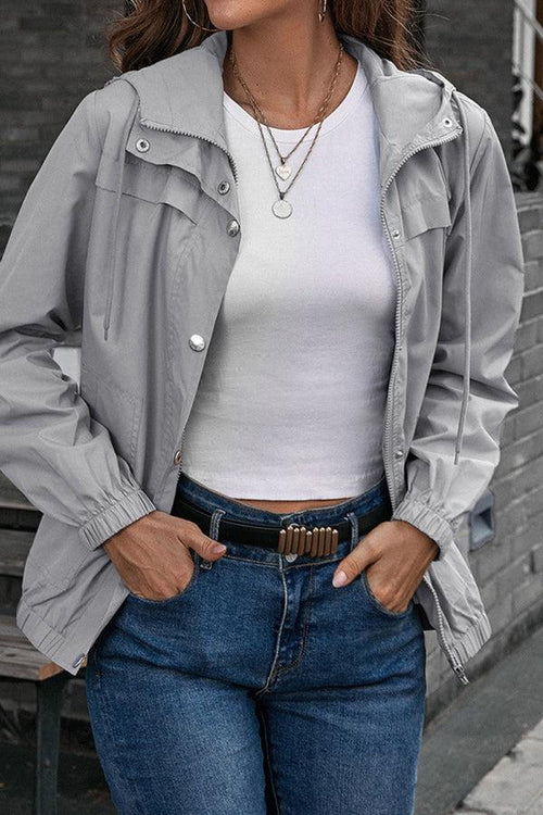 Woman wearing light grey outdoor hooded raincoat and windbreaker with white top and blue jeans