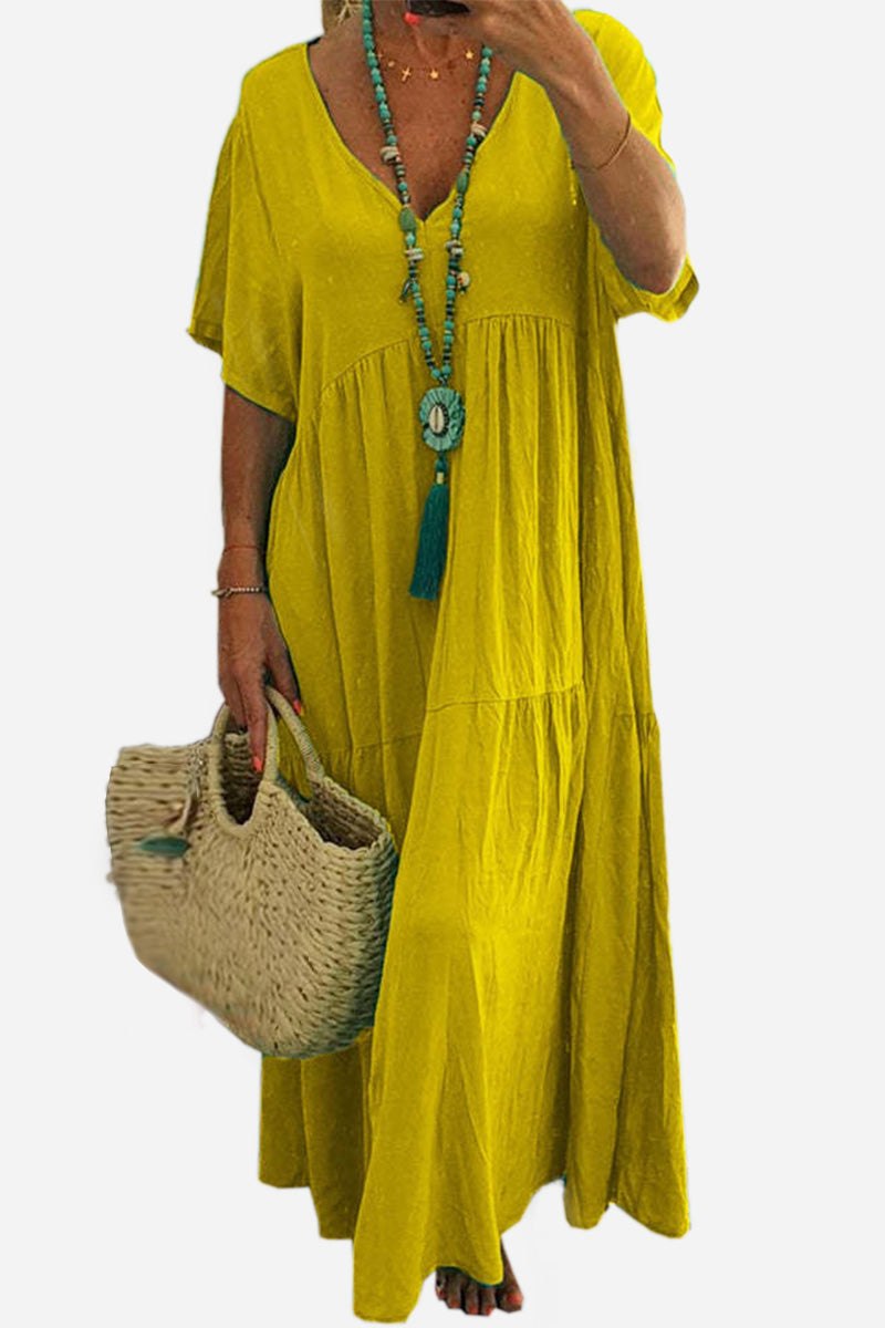 Yellow V-neck two-tiered maxi swing dress with loose sleeves and flowy silhouette worn with turquoise necklace and woven bag