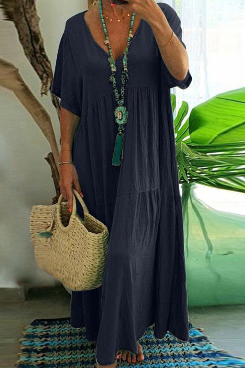 Woman wearing navy blue V-neck two-tiered maxi swing dress holding woven handbag with green leafy background