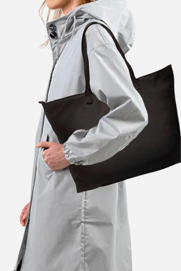 Waterproof travel bag in black with sturdy handles carried by person in gray raincoat