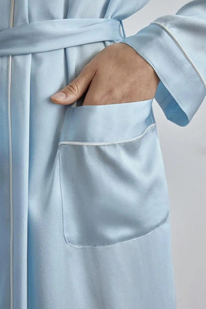 Close-up of hand in pocket of light blue Mulberry silk nightgown with sash belt and white piping detail