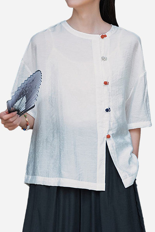 White regenerated cellulose blouse with asymmetrical colorful buttons and oversized fit worn by model holding a fan