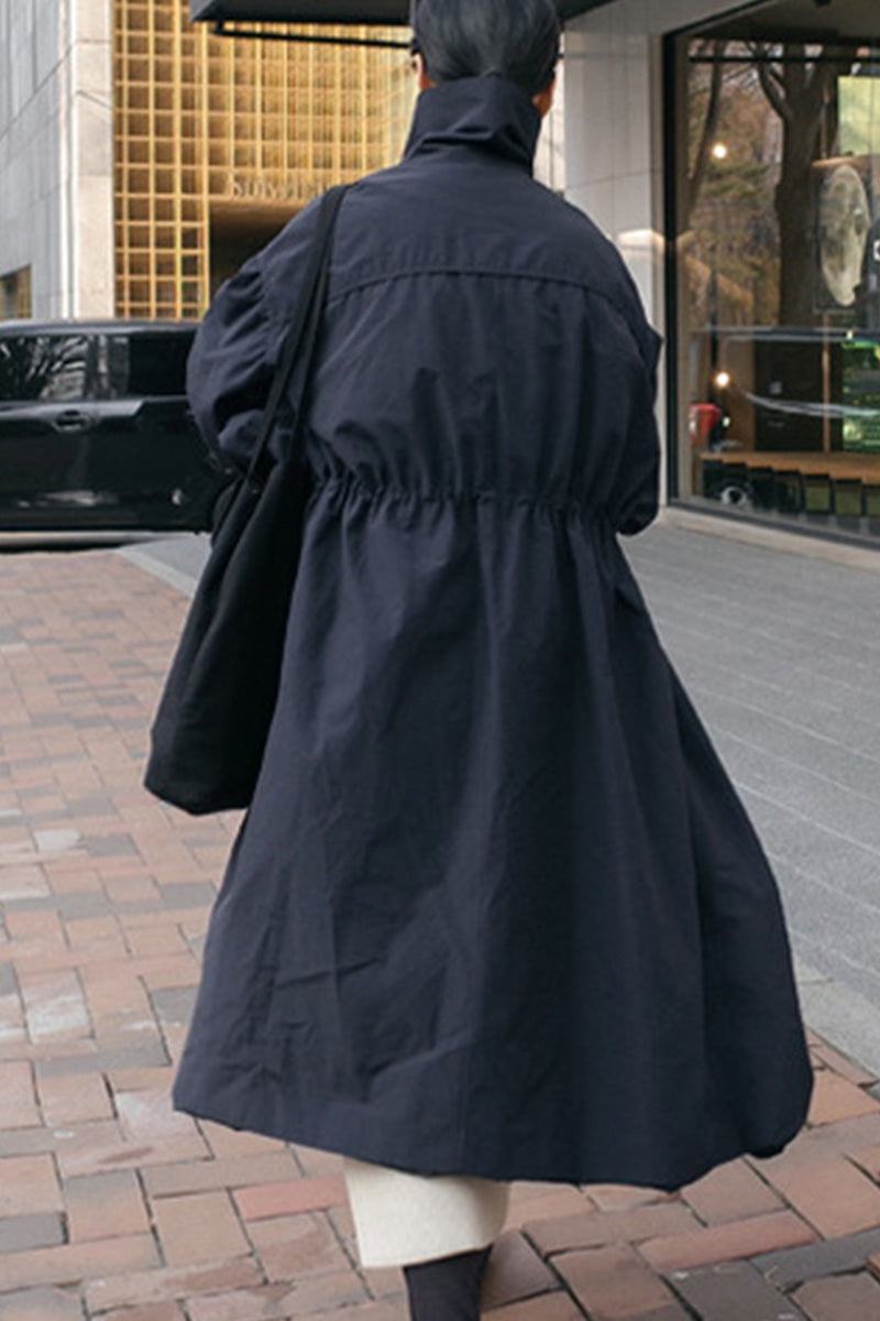 Back view of a person wearing a black oversized cotton stain-resistant coat, walking on an urban sidewalk.