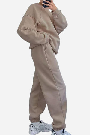 Woman wearing beige comfy chic tracksuit with relaxed fit and white sneakers against white background