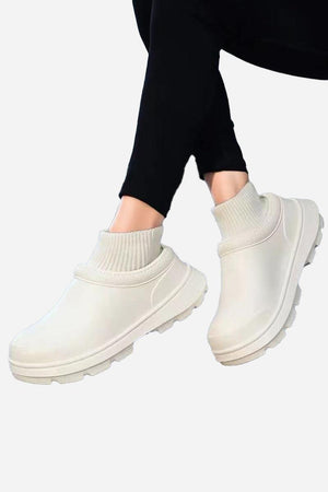 White fleece-lined comfort clogs with waterproof exterior and textured sole worn with black leggings