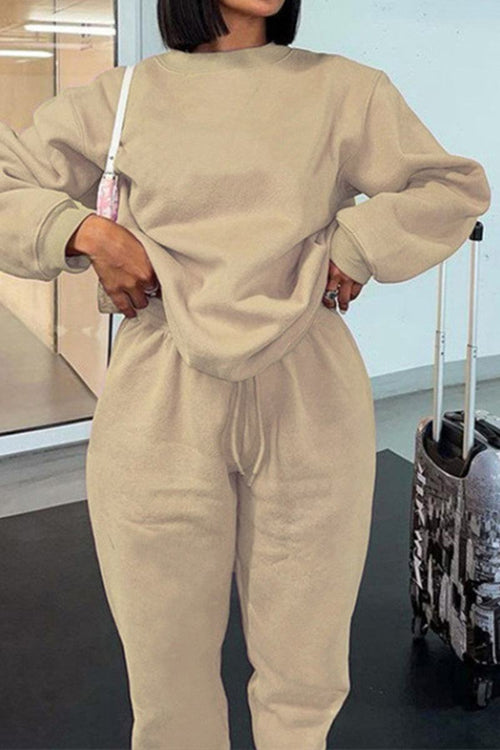 Woman wearing beige Classic Comfort Athleisure set with long sleeves and drawstring pants standing next to a suitcase
