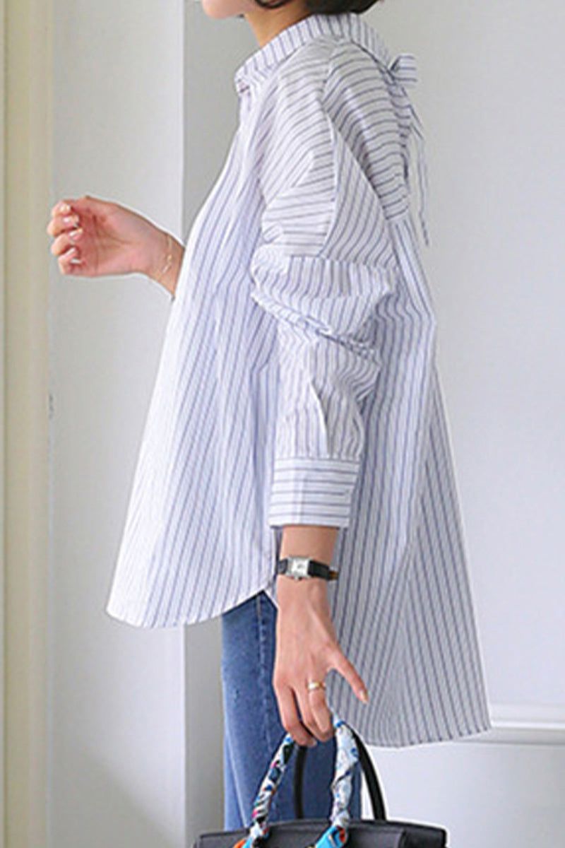 Side view of a person wearing a 100 cotton oversized striped shirt with rolled sleeves and blue jeans, holding a patterned handbag