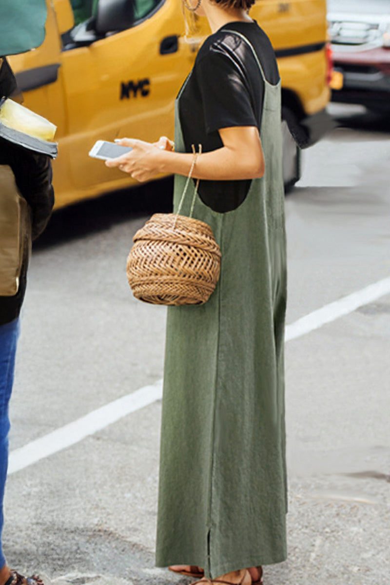 Woman wearing olive green cotton blend comfort jumpsuit with wide-leg design and black t-shirt underneath, carrying woven basket bag by street curb.