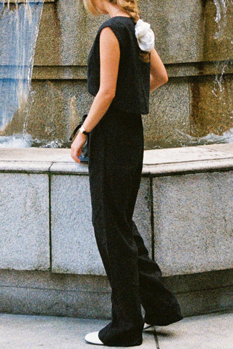 Woman wearing black cotton-linen blend two-piece outfit with wide-leg pants and sleeveless cropped top standing by water fountain