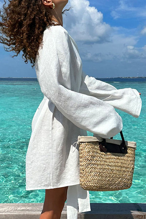 Woman wearing white cotton-linen blend spa robe by the ocean holding woven basket bag