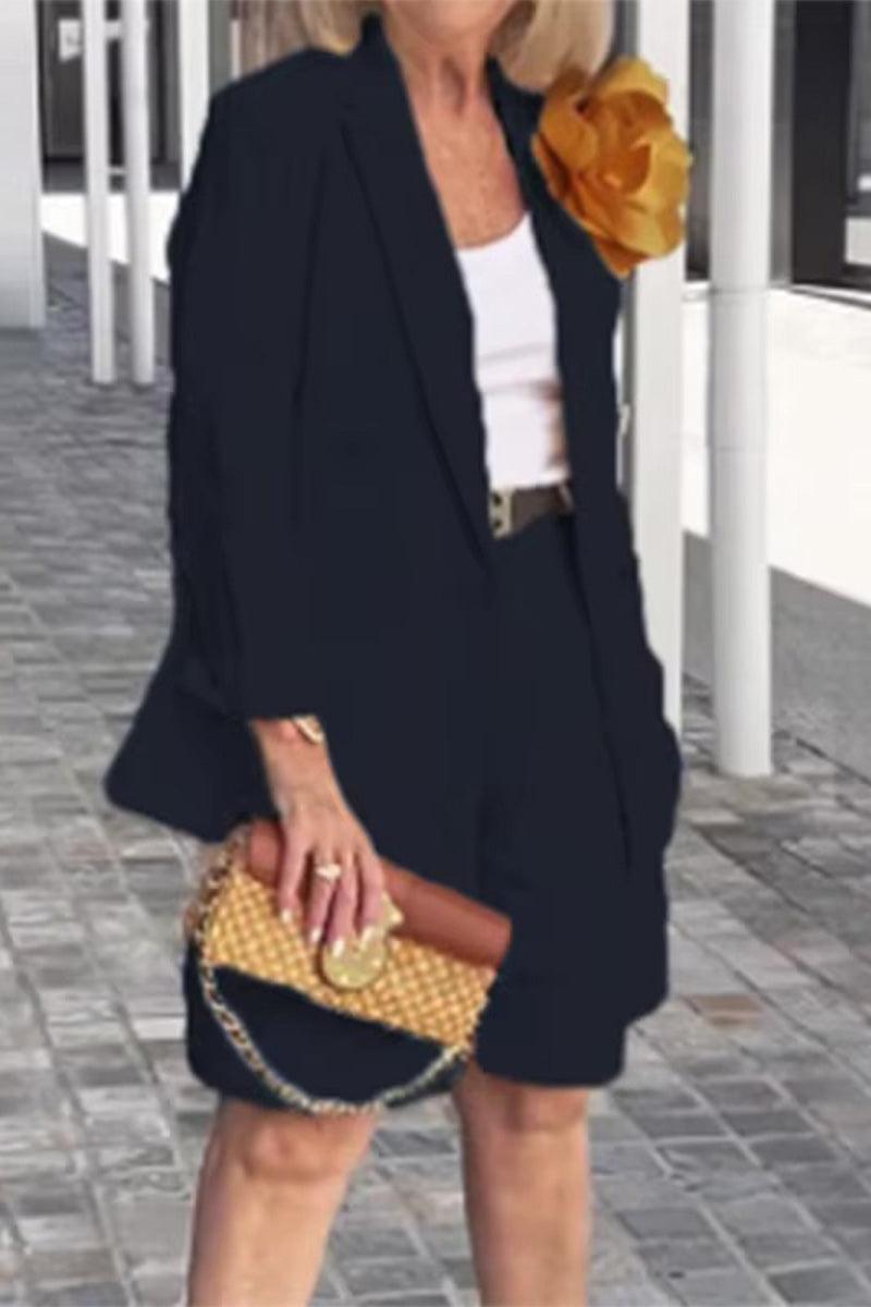 Woman wearing a stylish blazer and shorts two-piece set in black with a white top and a floral accessory.