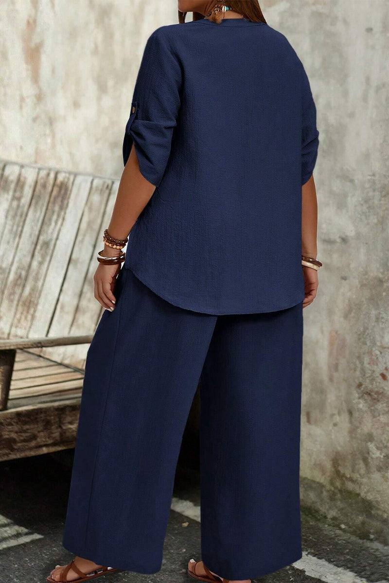 Woman wearing a navy wrinkle-free wide leg and top set with rolled-up sleeves standing outdoors.