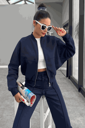 Woman wearing The Voyager Zip Set navy zip-front sweatshirt and wide-leg joggers with pockets, styled with white crop top and sunglasses.