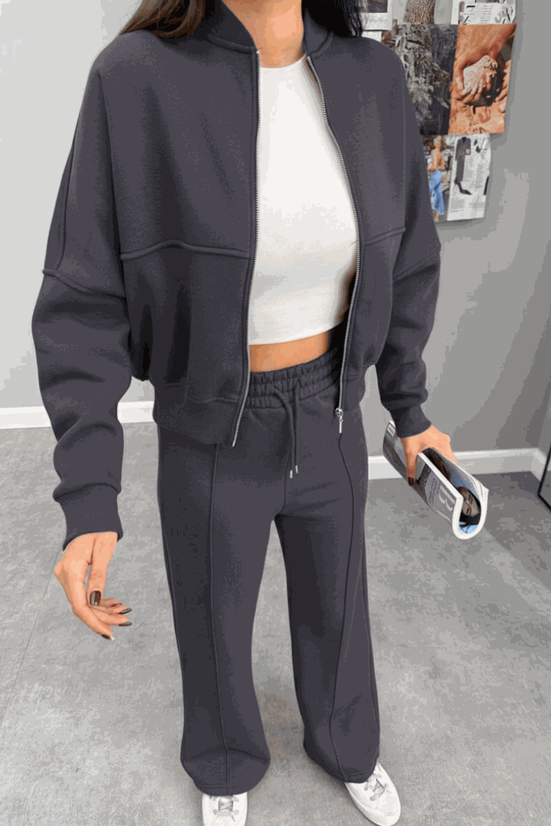 Woman wearing The Voyager Zip Set in dark gray with zip-front sweatshirt and wide-leg joggers, styled casually with a white crop top and sneakers.