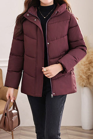 Woman wearing maroon Everyday Warmth Coat with hood and zip front, styled with black pants and handbag.