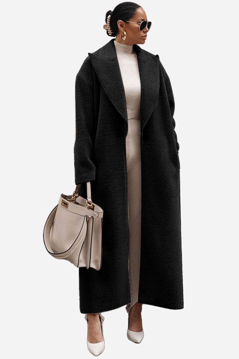 Woman wearing black oversized teddy coat with longline silhouette and drop shoulder design carrying beige handbag