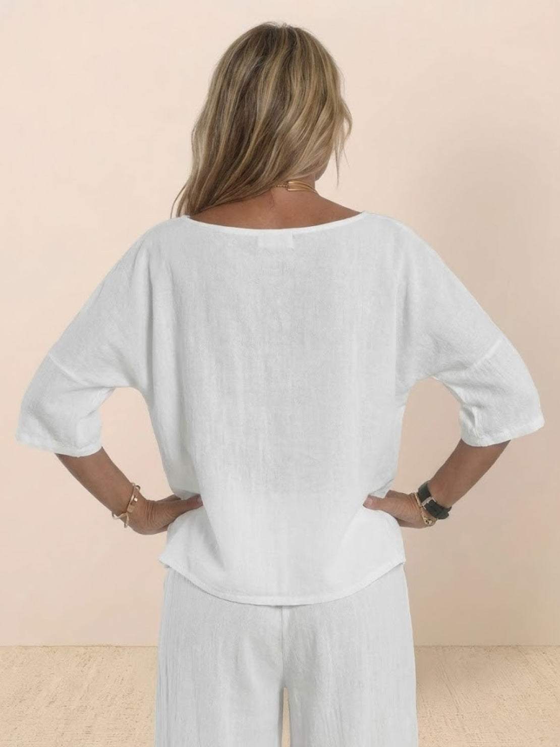 Back view of a woman wearing a white short-sleeved pullover and wide trouser matching set made of lightweight breathable cotton fabric.