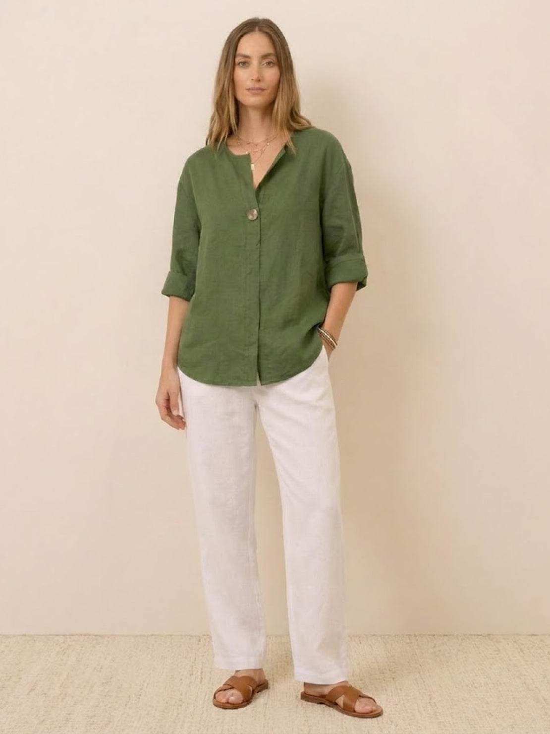 Woman wearing green Pure Linen Age-Defying Shirt with button detail, paired with white pants and sandals.