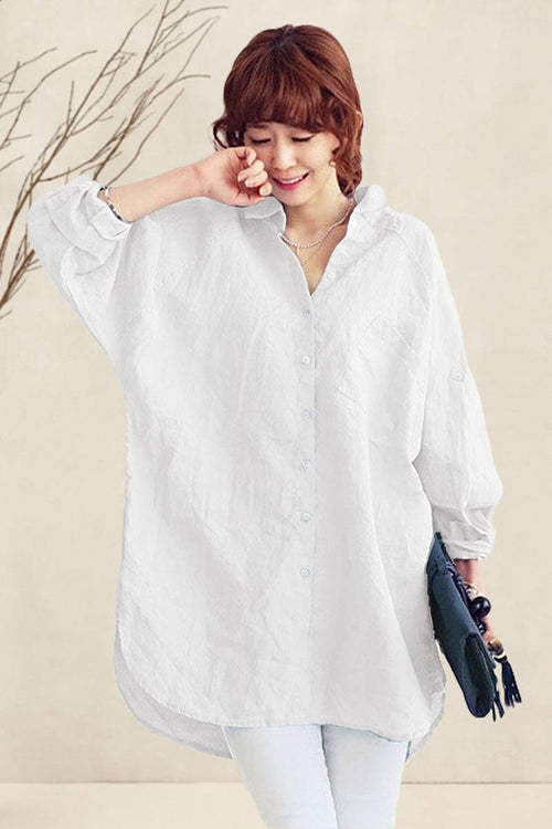 Woman wearing a white oversized linen shirt with relaxed fit and button details, styled casually with white pants and holding a clutch bag
