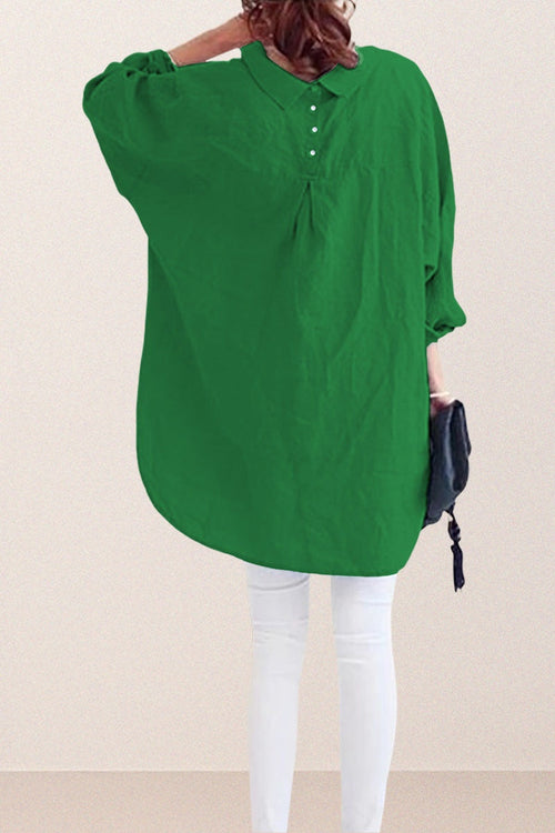 Back view of a woman wearing a green oversized linen shirt with gathered yoke and button details paired with white pants and holding a black clutch bag