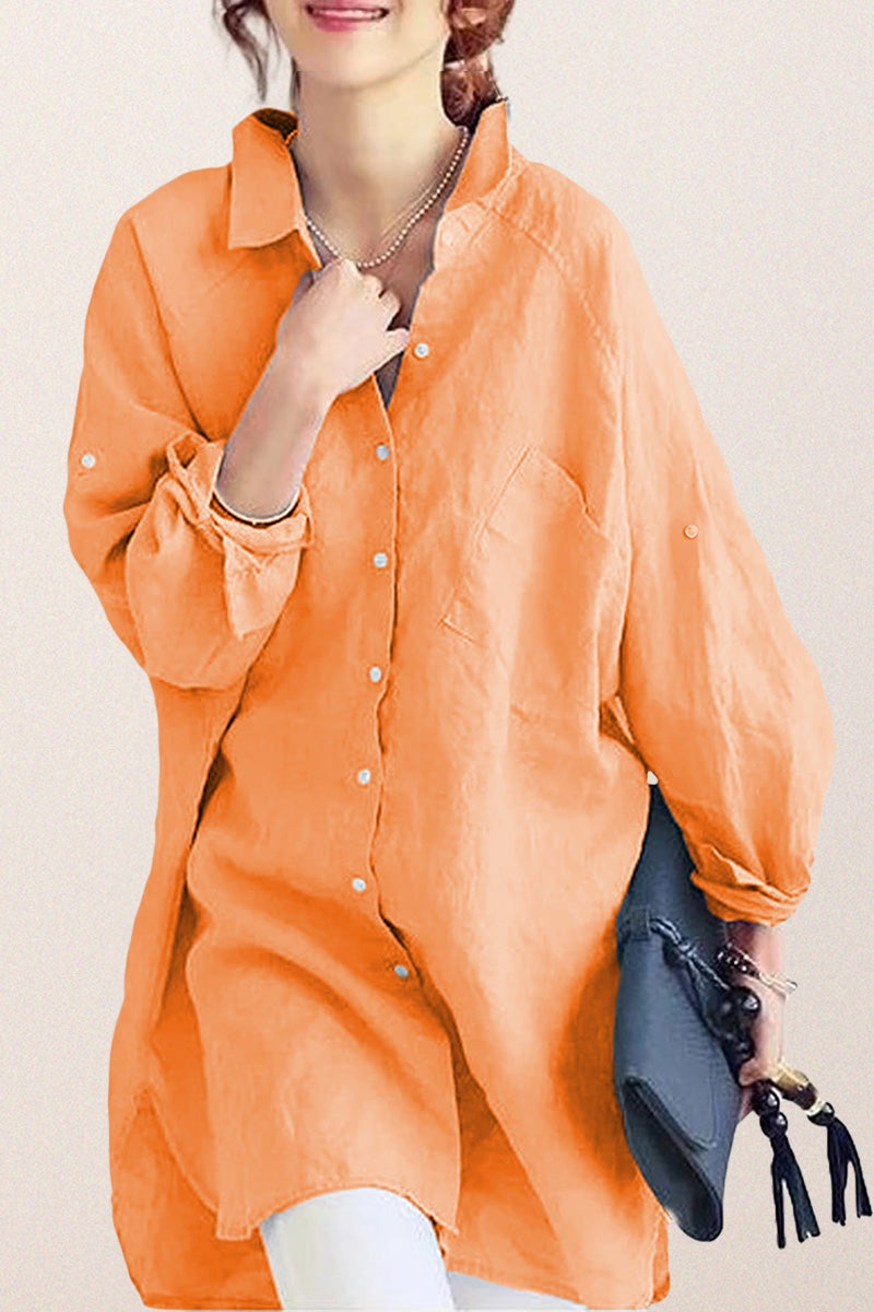 Woman wearing oversized orange linen shirt with rolled-up sleeves holding a gray clutch bag