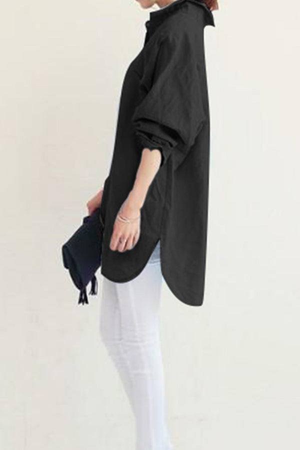 Black oversized linen shirt with rolled sleeves worn with white pants and holding a black clutch bag