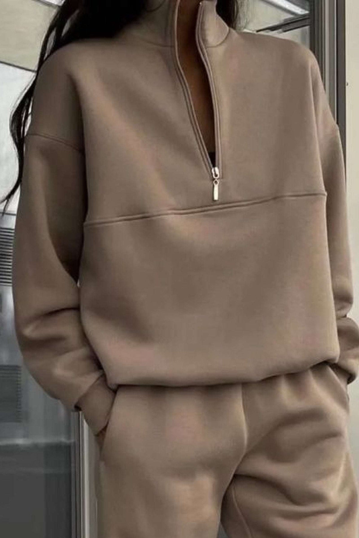 Woman wearing a neutral-toned cotton blend tracksuit with a high collar and half-zip pullover.