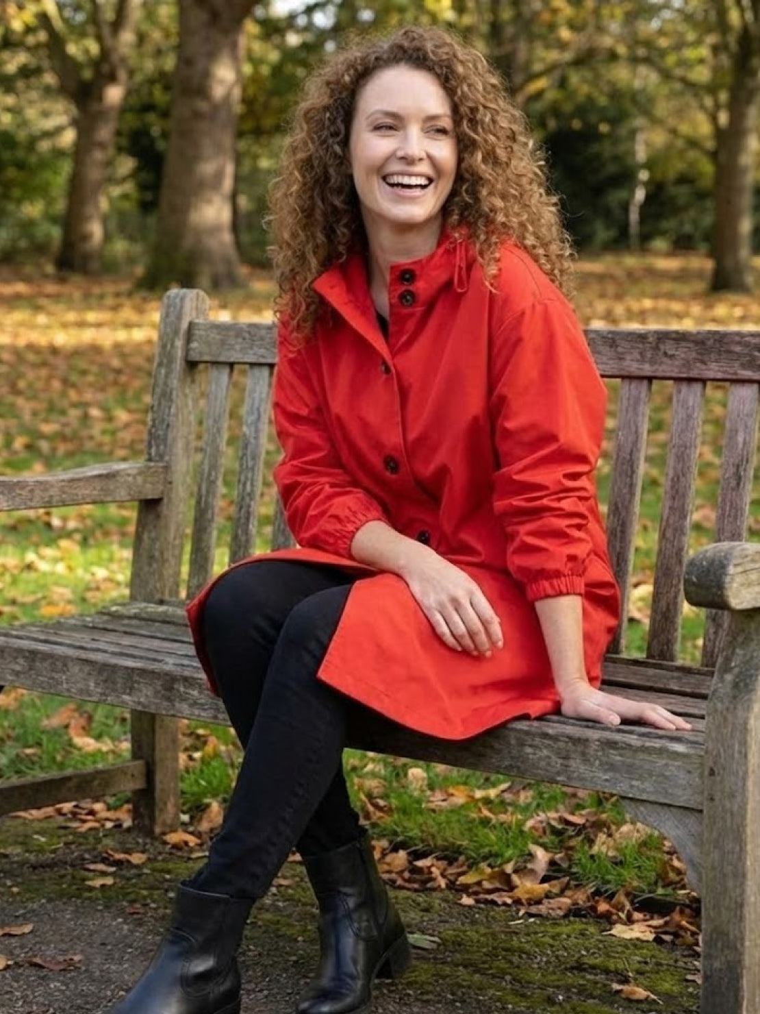 Woman wearing red Rain Couture Windbreaker sitting on park bench in autumn setting