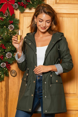 Woman wearing a dark green water resistant windbreaker jacket with hood standing indoors near Christmas decorations