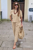Woman wearing beige relaxed fit cotton linen set with short-sleeve top and straight-leg pants carrying woven bag outdoors
