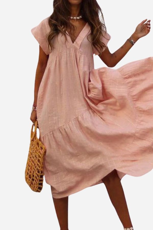 Woman wearing pink V neck tiered cotton midi dress with short sleeves and frill hem holding woven bag