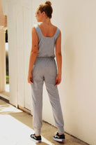Woman wearing comfy sleeveless vest pocket jumpsuit in light grey with elastic waistband and casual sneakers.
