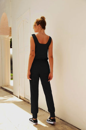 Woman wearing a black comfy sleeveless vest pocket jumpsuit with elastic waistband standing outdoors