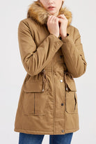 Woman wearing large hooded velvet coat with fur collar and front pockets in brown color