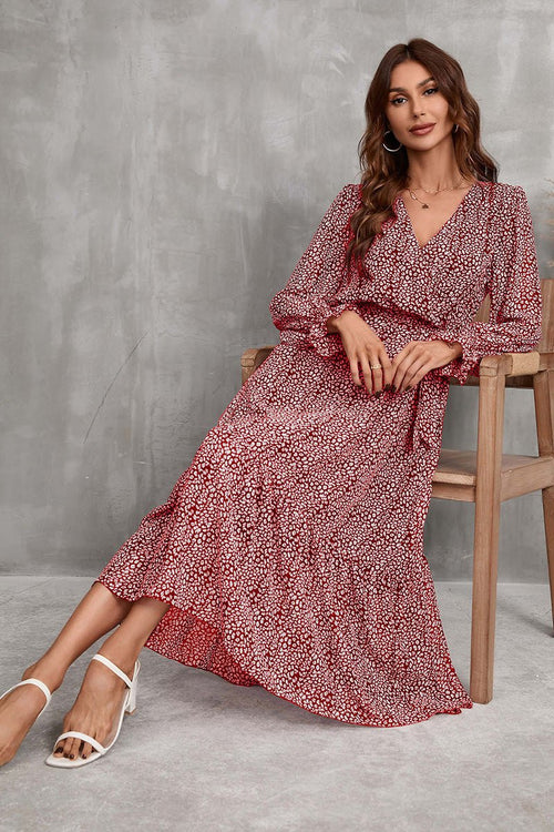 Woman wearing Bloom Wrap Midi Dress with floral print and trumpet sleeves sitting on wooden chair against gray background