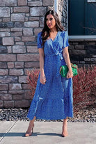 Woman wearing a blue charming floral boho maxi dress with short sleeves and a wrap V-neck standing outdoors near a stone wall.