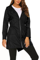 Outdoor and Travel Hooded Raincoat in black lightweight waterproof fabric with front zipper and pockets, worn by woman for travel and outdoor activities