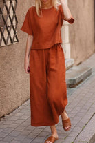 Woman wearing rust-colored loose fit co-ord set with short sleeves and wide-leg pants walking on a city sidewalk