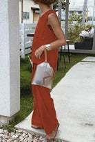 Woman wearing loose solid color sleeveless two-piece set in burnt orange with wide-leg pants and a silver handbag outdoors